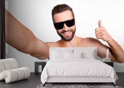 Self portrait of cheerful joyful lifeguard with stubble shooting selfie on front camera showing thumb up sign isolated on grey background Wall mural