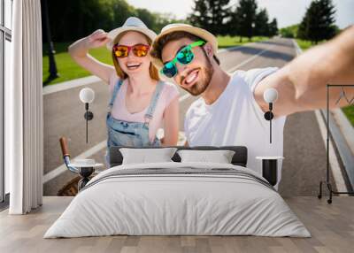 Self portrait of cheerful stylish brother and sister shooting selfie on front camera outdoor while riding on bikes enjoying holidays. Sun adventure photography concept Wall mural