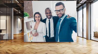 Self portrait of three partners, bearded man in glasses making selfie on front camera with his colleagues in classic suits, holding mug with tea in hand, standing in work place, station Wall mural