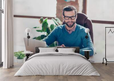 Stunning, smiling, harsh, virile, IT-manager in glasses, pullover, shirt, sitting on leather chair at desktop in workplace, looking at camera Wall mural