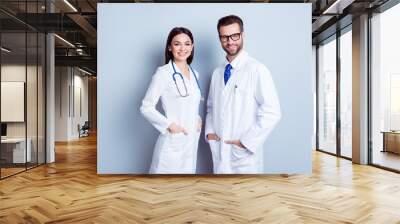 Two best smart professional smiling doctors workers in white coats holding their hands in pockets and together standing against gray background Wall mural