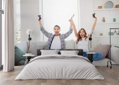 Two person nice attractive lovely cheerful cheery positive guy lady sitting on divan playing station having fun celebrating winning raising hands up in light white style interior room Wall mural