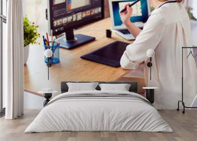 Vertical photo of attractive young photographer working with computer at the table and retouching with computer Wall mural