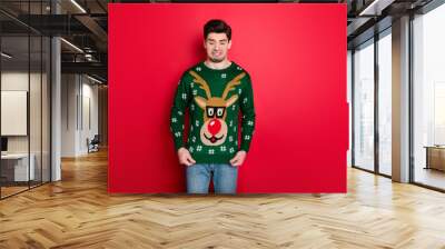 What a disgust. Portrait of frustrated man look at his funny ugly sweater dislike his christmas present wear denim jeans isolated over red color background Wall mural