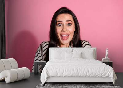 Young brunette woman in casual striped shirt expressing surprise against a vibrant pink background Wall mural