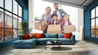 Young happy smiling family four persons wearing casual standing together holding carton boxes with stuff things in light living room moving to new flat Wall mural