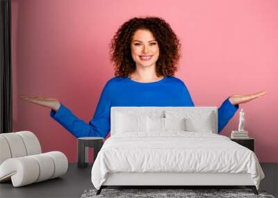 Young woman with curly hair in casual blue sweatshirt smiling against pink background for advertising and promotion Wall mural