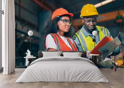 Two professional engineer/worker/technician use clipboard discuss work, walk in steel metal manufacture factory plant industry. Black African American man and woman wear hard hat check quality machine Wall mural