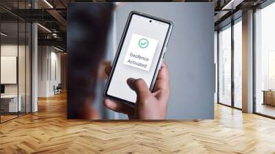 Man hand holding phone. Mobile screen showing he finished geofence activation steps successfully. Selective focus, location based services, virtual perimeter settings concept. Wall mural