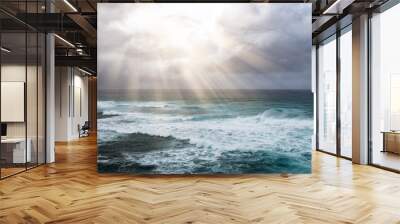 Rays of sunlight break through storm clouds above the open ocean waves in a heavenly seascape Wall mural