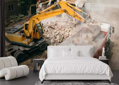 Excavator breaks building and loads construction waste into truck with its bucket. Demolition of building. Wall mural