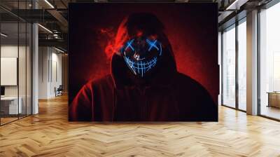 Man in angry and scary lighting neon glow mask in hood on dark red background. Halloween and horror concept Wall mural