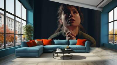 Portrait of young woman at home looks up, praying and whispering in dark room. Religion hope and faith concept. Wall mural