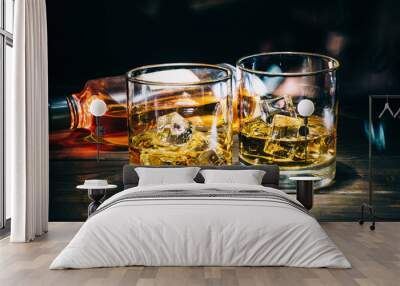 Two glasses of scotch whiskey or cognac with ice cubes and bottle of alcohol liquor on dark wooden background Wall mural