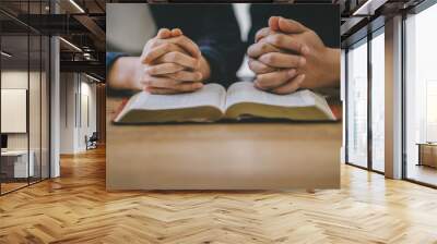 Christian group of people holding hands praying worship to believe and Bible on a wooden table for devotional or prayer meeting concept. Wall mural