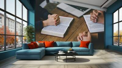 Christian group of people holding hands praying worship to believe and Bible on a wooden table for devotional or prayer meeting concept. Wall mural