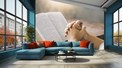 Christian hands folded for prayer with a holy bible on a wooden table in church for worship to god in the morning. person pray with faith, Spirituality, and religion concept Wall mural