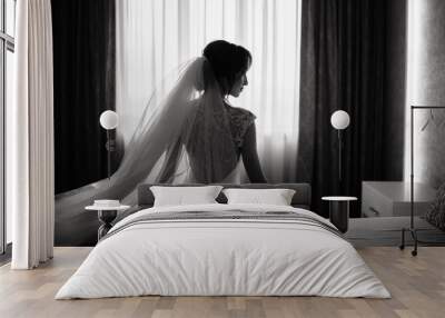 Elegant bride in a wedding dress sits on a bed in a hotel in front of window. Wedding morning of the bride. Wall mural