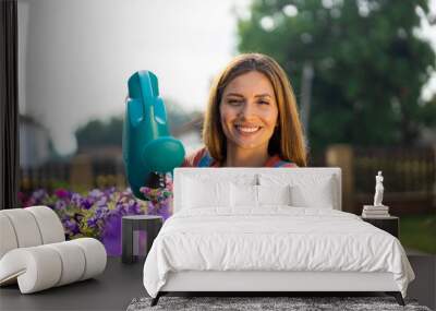 a beautiful woman is watering flowers in a pot on the terrace fence of a family house and look at camera Wall mural