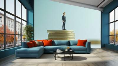 A miniature businessman stands atop a stack of gold coins, symbolizing financial success and wealth. Wall mural