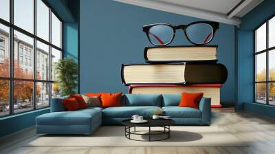 A stack of three hardback books with a pair of glasses on top, against a blue background. Wall mural