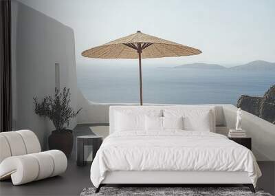 A table with two chairs and a straw umbrella on a white patio overlooking the sea. Wall mural