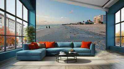 Wide angle view of Pass-a-grille beach in St. Pete Beach Florida looking north. Two people on left walking in the sand, Near sunset with green plants, blue water and white clouds. Waves and clouds Wall mural