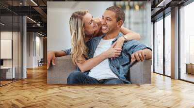 Love, happy and smile with a diversity couple hugging on a sofa in the living room of their home together. Support, romance and affection with a man and woman sharing an intimate moment in a house Wall mural