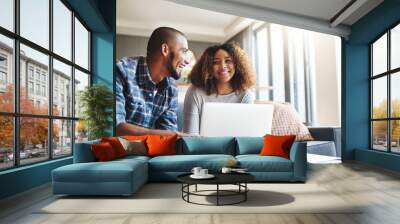 Happy, excited and cheerful couple browsing on laptop and using the internet for payments and calculating home budget while sitting on sofa. Young husband and wife enjoying convenient online banking Wall mural