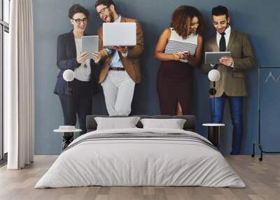 Happy workers using digital devices standing together on a work break. Group of relaxed employees using technology, a phone, computer and tablet. Office business team enjoying social media indoors Wall mural