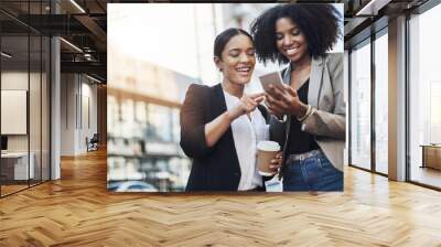 Reaching out to new networks. Shot of two businesswomen looking at something on a cellphone in the city. Wall mural