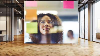 Thinking critically to create success. Shot of a young woman having a brainstorming session with sticky notes at work. Wall mural