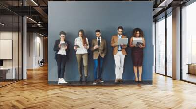 Waiting it out in the name of success. Studio shot of a group of businesspeople using wireless technology while waiting in line against a gray background. Wall mural