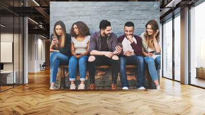 Whats life without friends and wifi. Shot of a group of young friends using their mobile phones outdoors. Wall mural