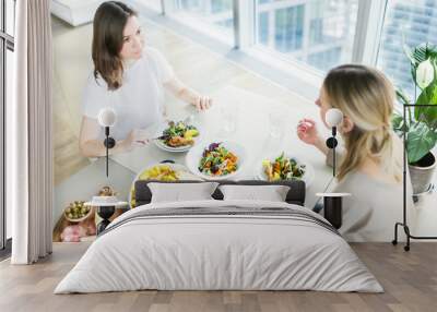 Young women eating together at the table in modern apartment. Top view Wall mural