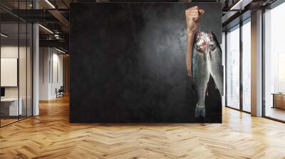 Crop cook holding hook with fresh raw fishes on black background Wall mural