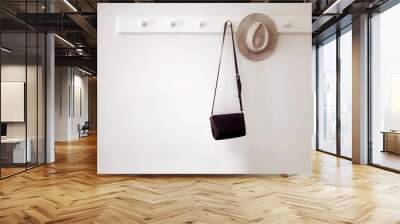 Stylish hat and small black purse hanging on white pegs on wall in cozy room Wall mural