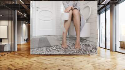 Woman sitting on the toilet holding toilet paper in her hands Wall mural