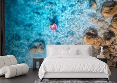 Aerial view of a young woman swimming with pink swim ring in blue sea at sunset in summer. Tropical landscape with girl, clear water, stones, sandy beach. Top view. Vacation in Lefkada island, Greece Wall mural