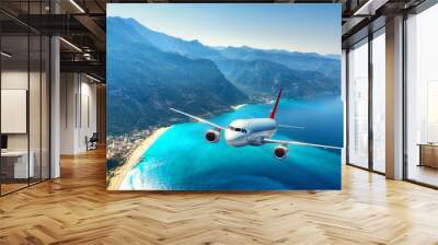 Airplane is flying over amazing mountains with forest and sea at sunrise in summer. Landscape with white passenger airplane, sky, islands and blue water. Passenger aircraft. Travel and resort. Tourism Wall mural