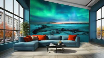 Aurora borealis over rocky beach and ocean. Northern lights in Teriberka, Russia. Starry sky with polar lights. Night winter landscape with aurora, sea with stones in blurred water, snowy mountains Wall mural