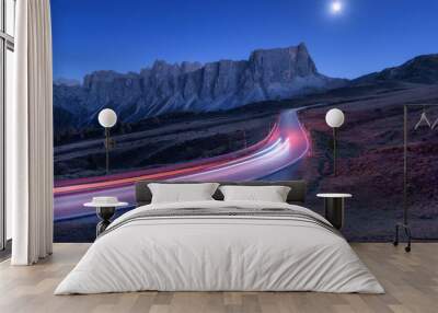 Blurred car headlights on winding road at night in autumn. Landscape with asphalt road, light trails, mountains, hills, blue sky with moonlight at dusk. Roadway in Italy. Moon over highway and rocks Wall mural