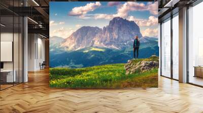 Girl on the hill with yellow flowers and green grass in beautiful alpine mountain valley at sunset in summer. Landscape with young woman in alps, sky with clouds, rocks. Travel in Dolomites, Italy Wall mural