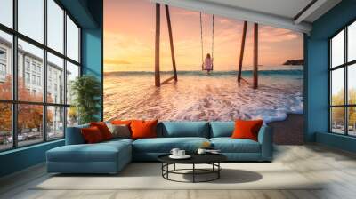 Happy young woman on wooden swing in water, beautiful blue sea with waves, sandy beach, orange sky at sunset. Summer holiday in Oludeniz, Turkey. Girl ride on a swing on sea coast, clear water. Travel Wall mural