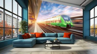 High speed train in motion at the railway station at sunset in Europe. Beautiful green modern train on the railway platform with motion blur effect. Industrial scene with passenger train on railroad Wall mural