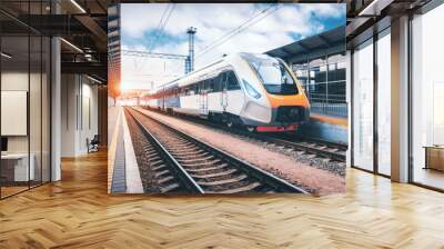 High speed train on the railway station at sunset. Industrial landscape with modern intercity passenger train on the railway platform and blue cloudy sky. Railroad in Europe. Commercial transportation Wall mural