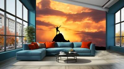 Landscape with silhouette of a standing happy man with backpack and raised-up arms on the mountain peak on the background of cloudy sky at colorful sunset in summer. Travel, Climbing, Trekking. Wall mural