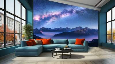 Milky Way above mountains in fog at night in autumn. Landscape with alpine mountain valley, low clouds, purple starry sky with milky way, city illumination. Aerial. Passo Giau, Dolomites, Italy. Space Wall mural