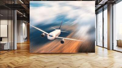 Modern airplane with motion blur effect is flying over low clouds at sunset. Passenger airplane, blurred clouds, forest, sunlight in dusk. Passenger aircraft. Business travel. Commercial plane.Concept Wall mural