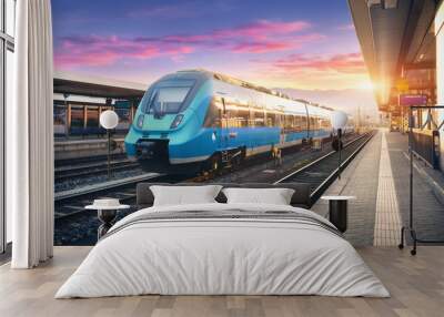 Modern high speed commuter train on the railway station and colorful sky with clouds at sunset in Europe. Industrial landscape with blue passenger train on railway platform. Railroad background Wall mural